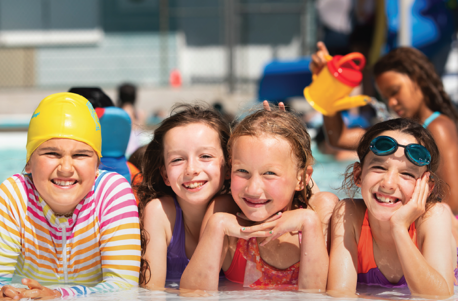 Children smiling at a poolside, wearing colorful swimwear and goggles.